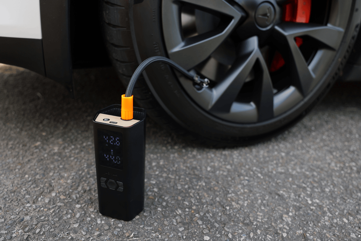Der Luftkompressor steht am Rad eines Tesla und pumpt den Reifen über den angeschlossenen Schlauch auf