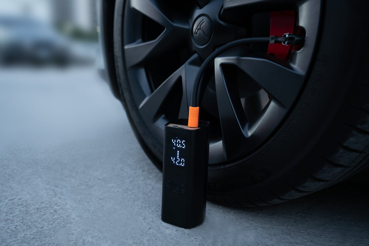 Luftkompressor am Reifen eines Tesla mit Blick auf das beleuchtete Druckdisplay
