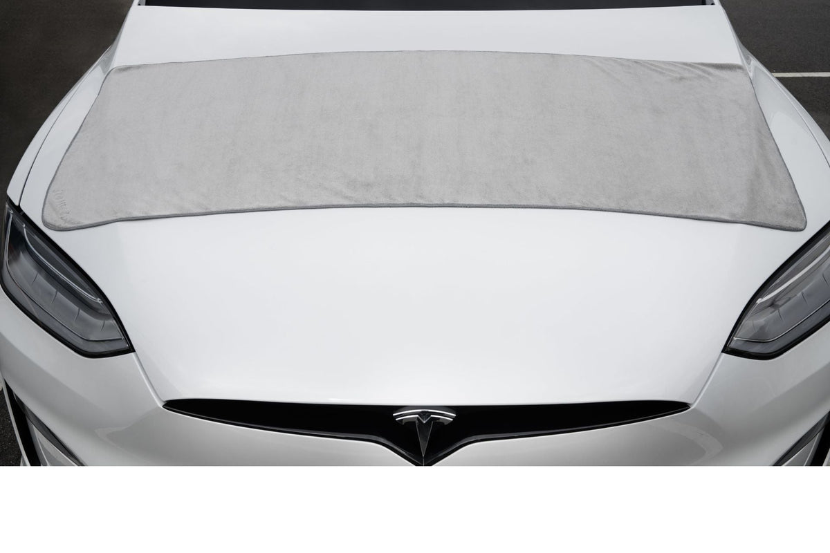 Das große Tuch auf der Fronthaube eines weißen Tesla, deckt die Haubenbreite in einem Zug ab