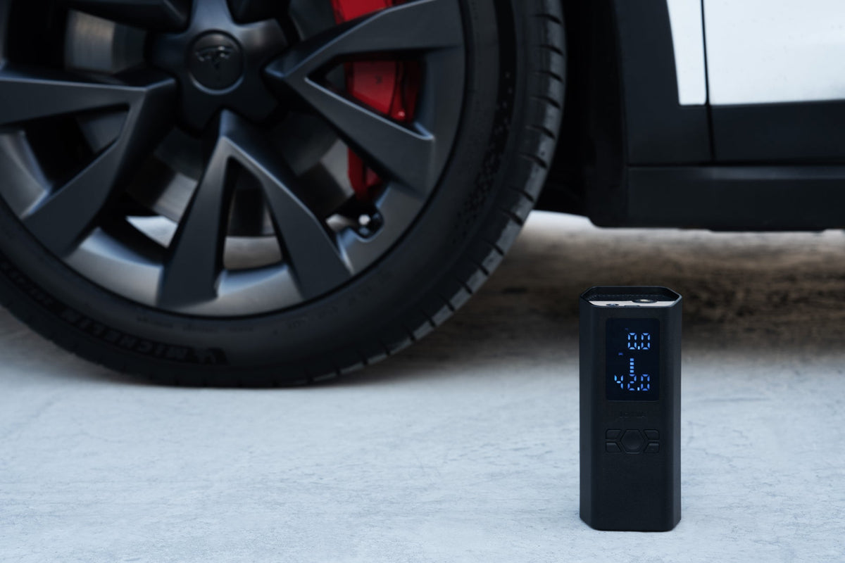 Der tragbare Luftkompressor steht neben dem Rad eines Tesla auf dem Asphalt